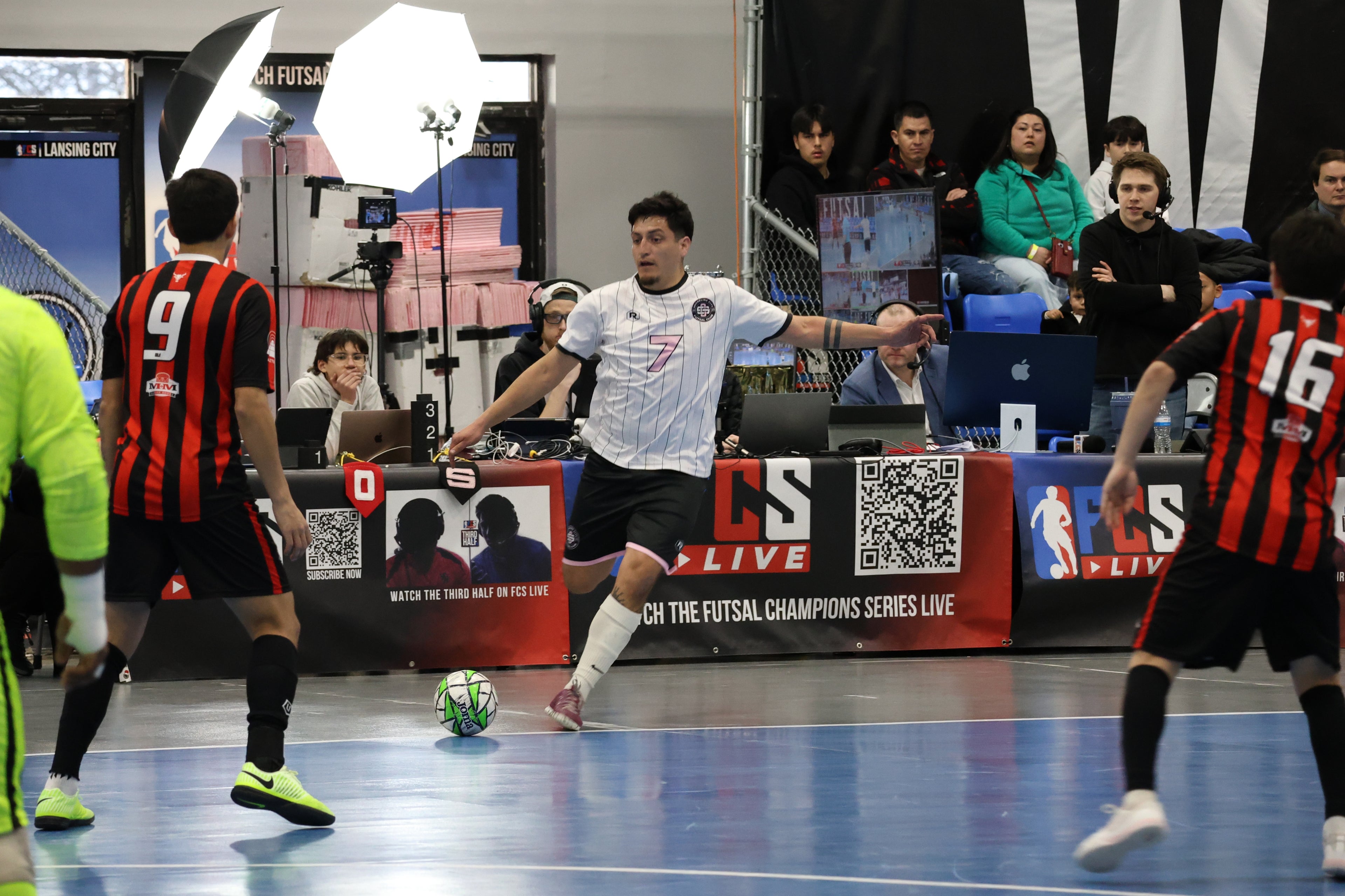 Futsal match in progress with players on a court, spectators in the background, and promotional banners.